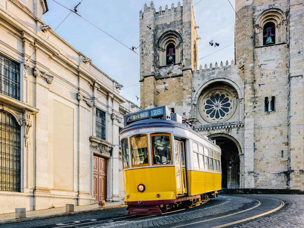 A yellow tram passing in front of Santa Maria cathedral in Lisbon